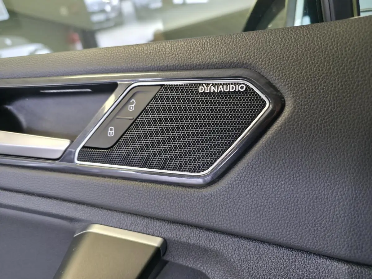 Gros plan sur l'enceinte Dynaudio intégrée à la porte intérieure en simili-cuir noir du Volkswagen Tiguan gris.