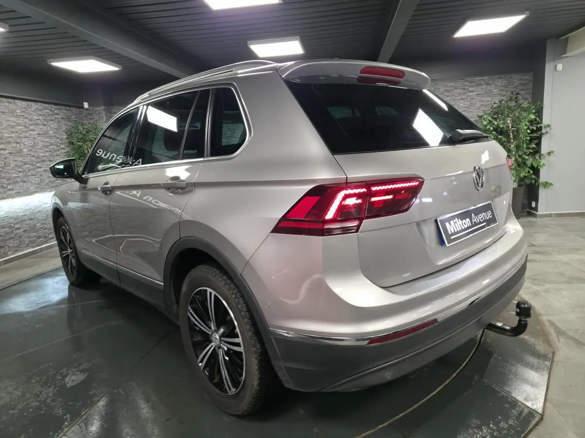 Vue 3/4 arrière droit d'un Volkswagen Tiguan gris métallisé avec jantes alliage noires et crochet d'attelage démontable.