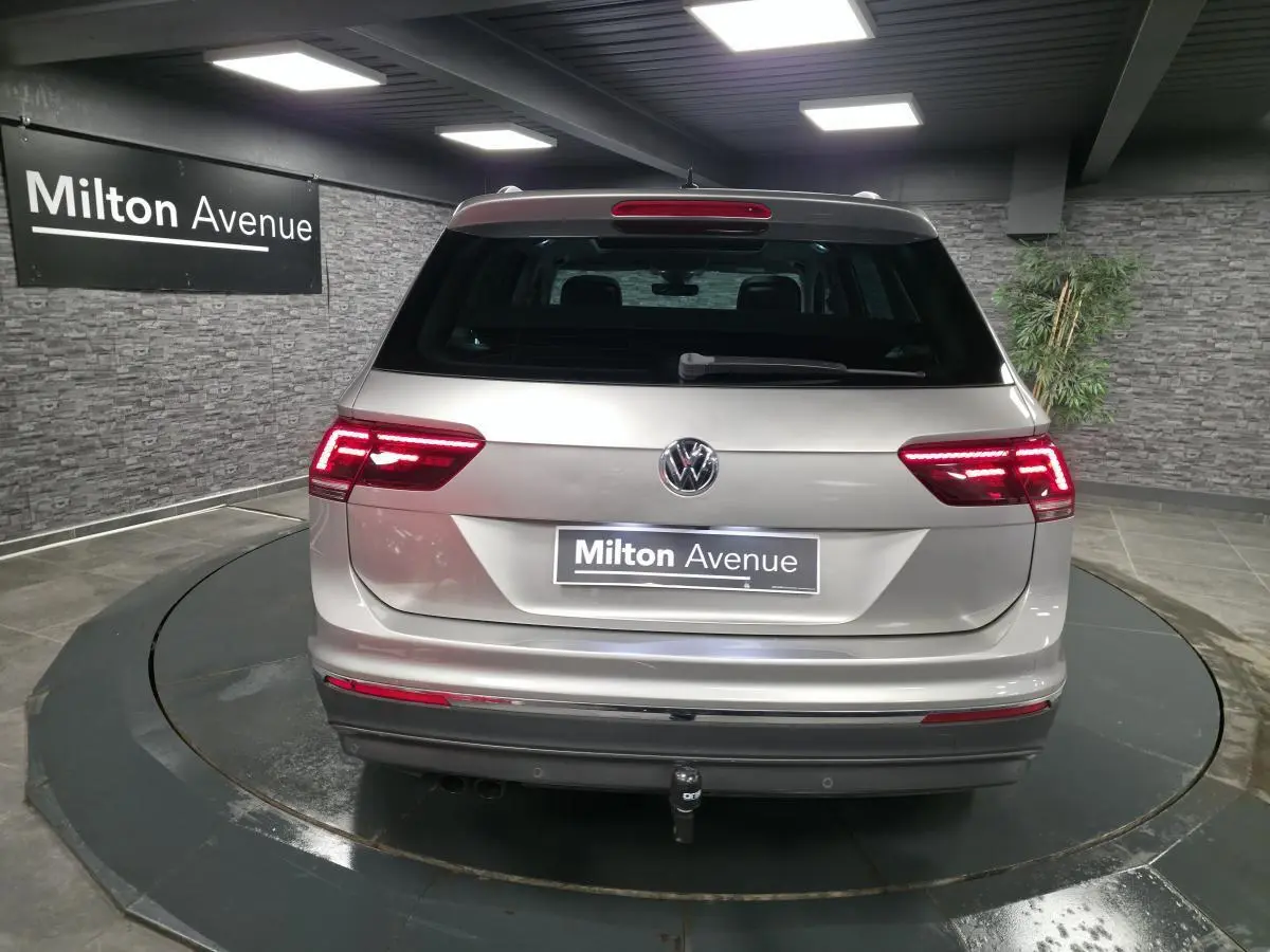 Vue arrière d'un Volkswagen Tiguan gris métallisé avec feux LED allumés et crochet d'attelage visible en intérieur showroom.