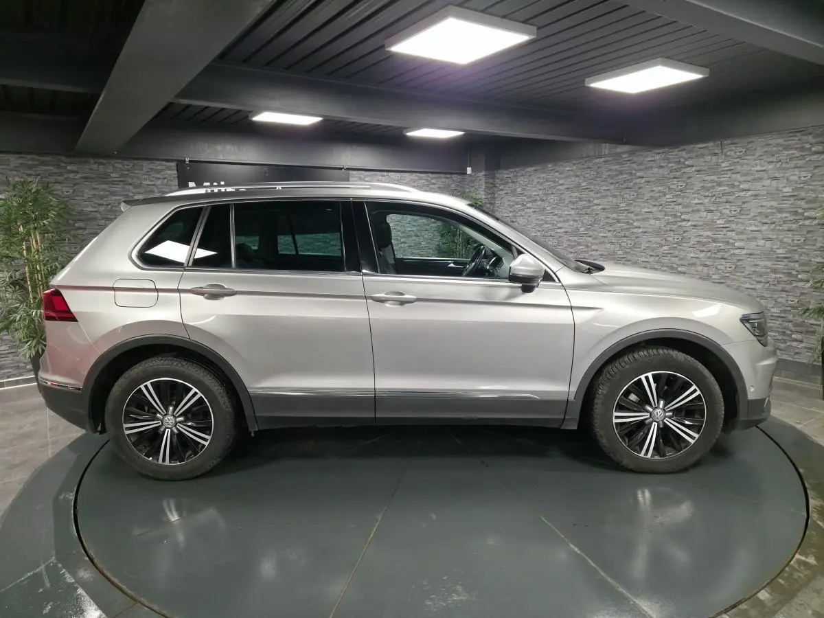 Volkswagen Tiguan gris métallisé vu de profil côté gauche avec jantes alliage noires et toit ouvrant panoramique.