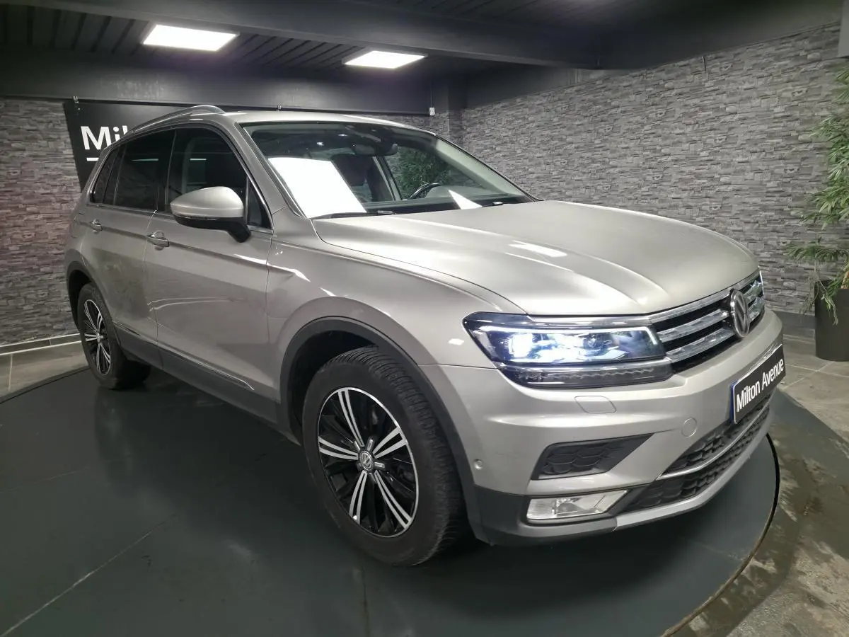 Volkswagen Tiguan gris métallisé vu en 3/4 avant droit avec phares allumés et jantes alliage noires.