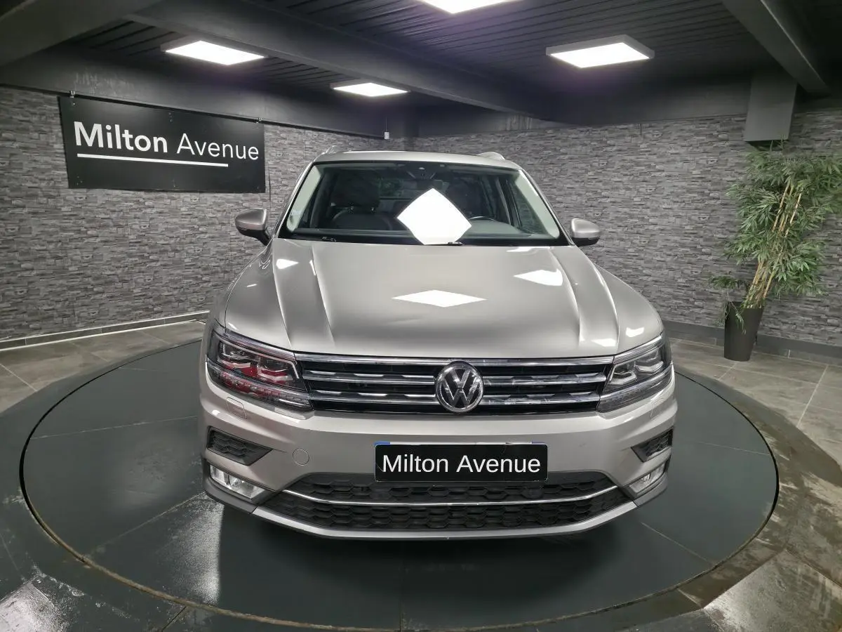 Vue frontale d'un Volkswagen Tiguan gris métallisé dans un showroom avec éclairage intérieur et panneau Milton Avenue.
