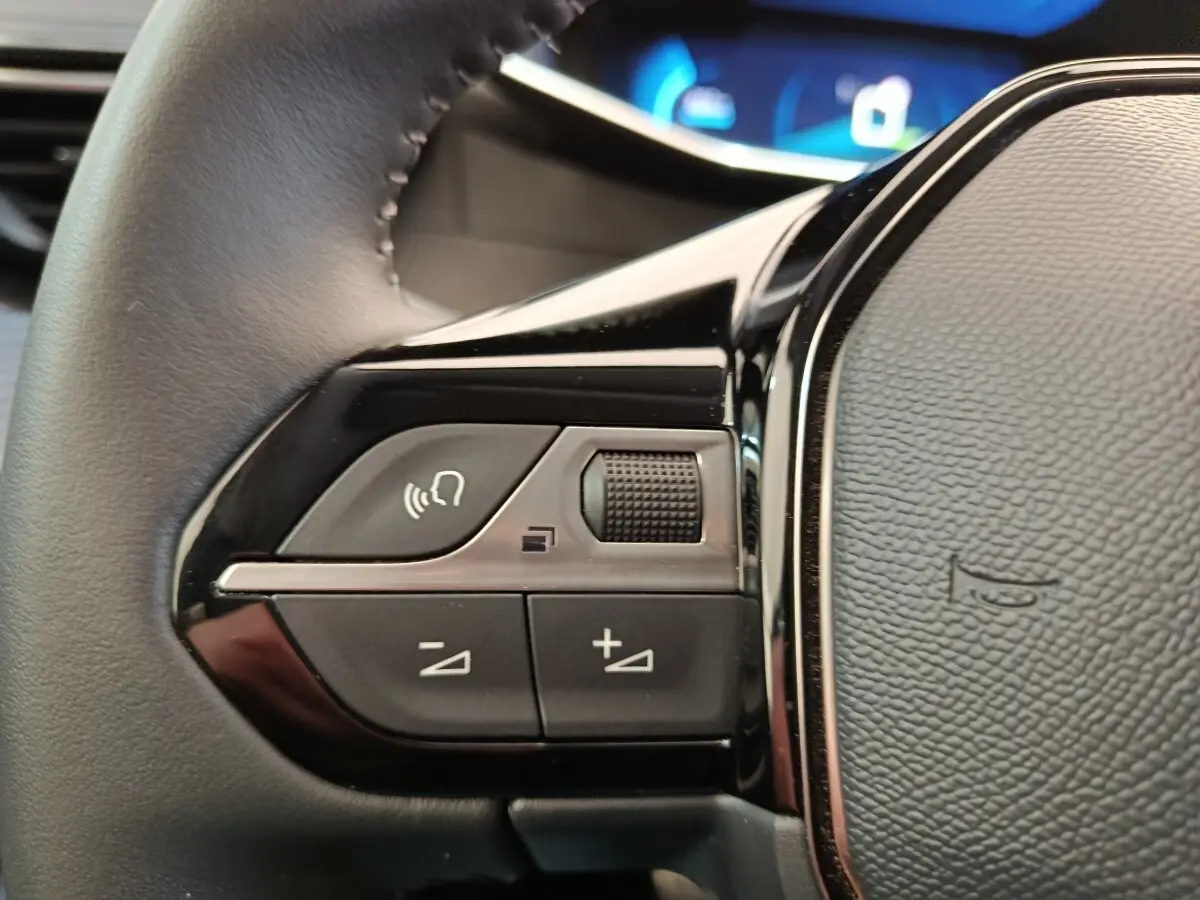 Gros plan sur les commandes vocales et volume au volant cuir noir de la Peugeot 208 électrique gris clair 2022.