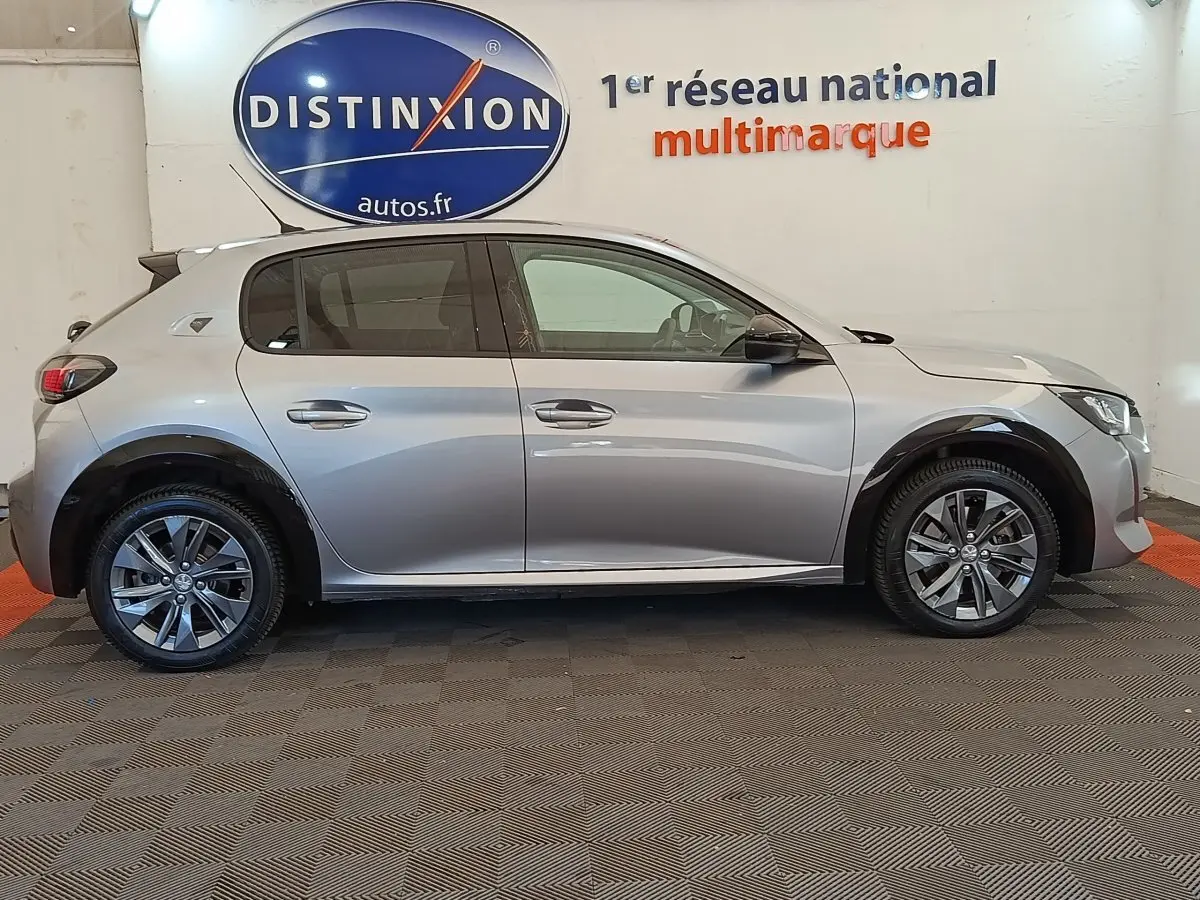 Vue de profil droit d'une Peugeot 208 Electrique ROADTRIP gris clair, avec jantes alliage et protections noires sur les passages de roues.