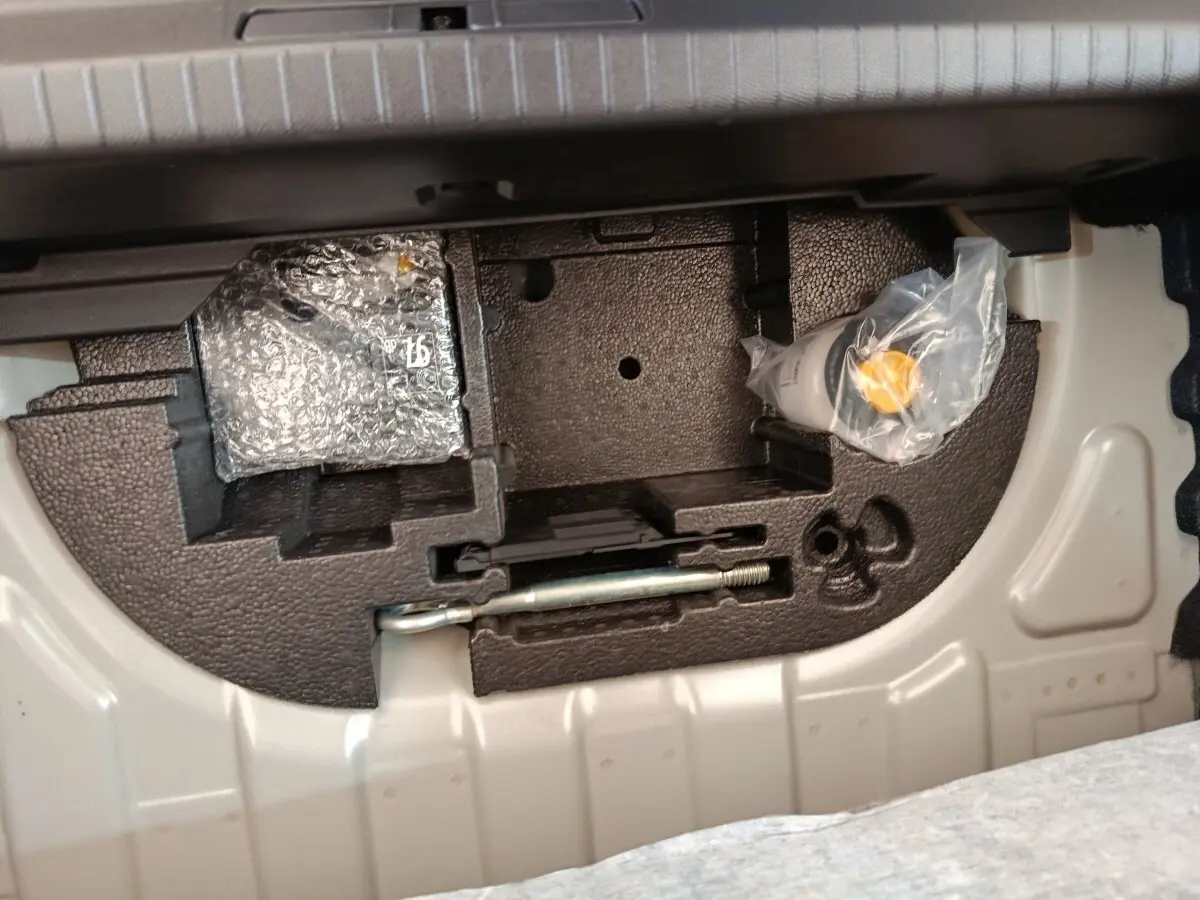 Compartiment de rangement sous le plancher de coffre de la Peugeot 208 électrique gris clair, avec outils et accessoires emballés.