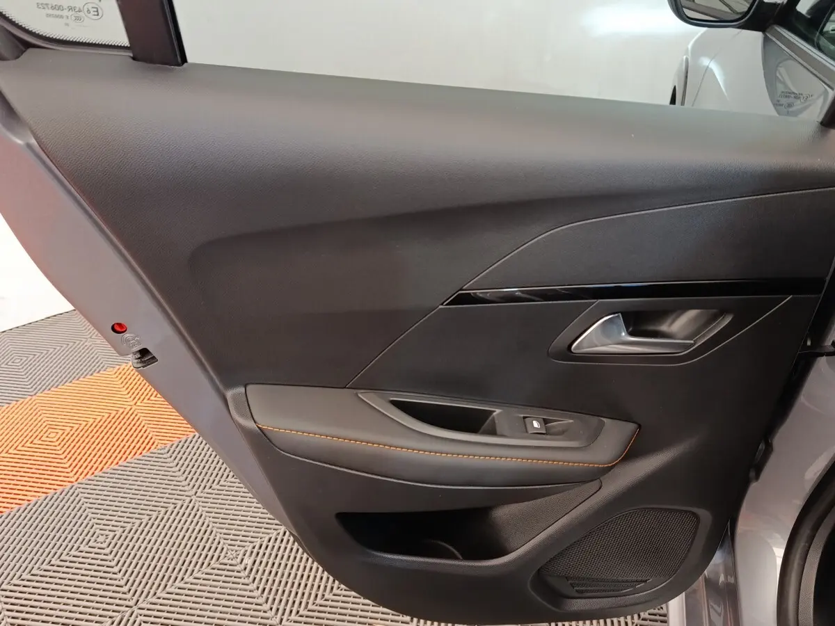 Intérieur côté gauche de la porte avant d’une Peugeot 208 électrique gris clair avec surpiqûres orange.