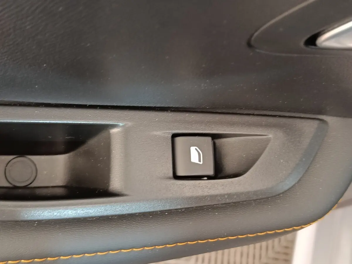 Gros plan sur le bouton de commande de la vitre, intérieur noir avec surpiqûres orange, Peugeot 208 électrique gris clair.