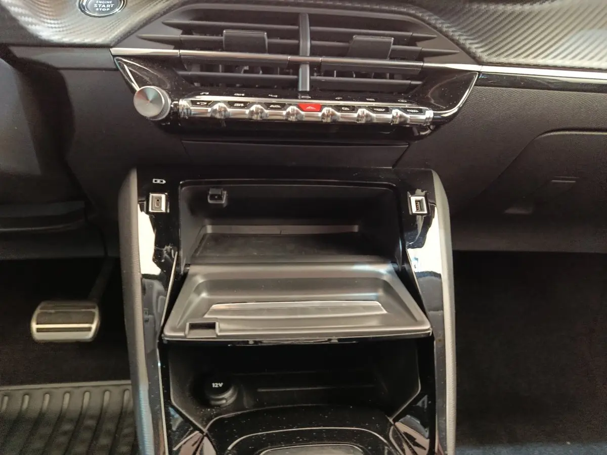 Vue rapprochée du tableau de bord central noir brillant de la Peugeot 208 Electrique ROADTRIP 2022, avec commandes et prises USB visibles.