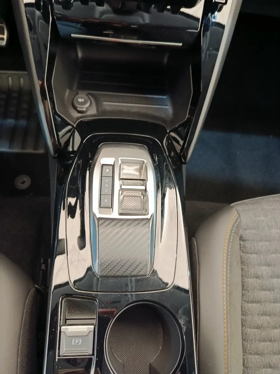 Vue plongeante sur la console centrale noire brillante de la Peugeot 208 électrique avec levier de vitesse automatique et frein à main électrique.