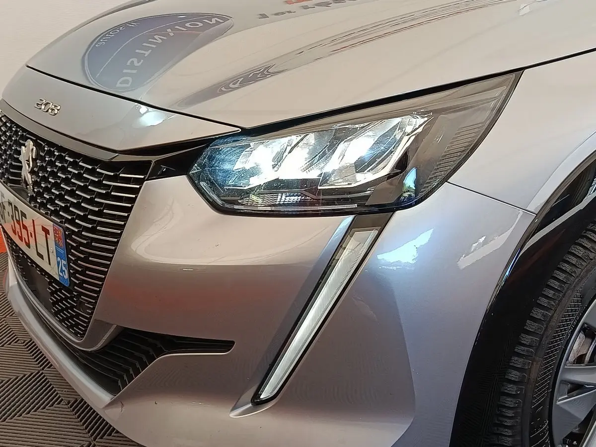 Gros plan sur l'avant droit gris clair de la Peugeot 208 Electrique ROADTRIP 2022 avec phares LED allumés et calandre noire.