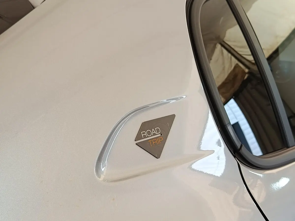 Détail du logo Roadtrip sur la porte arrière côté droit d’une Peugeot 208 électrique gris clair.