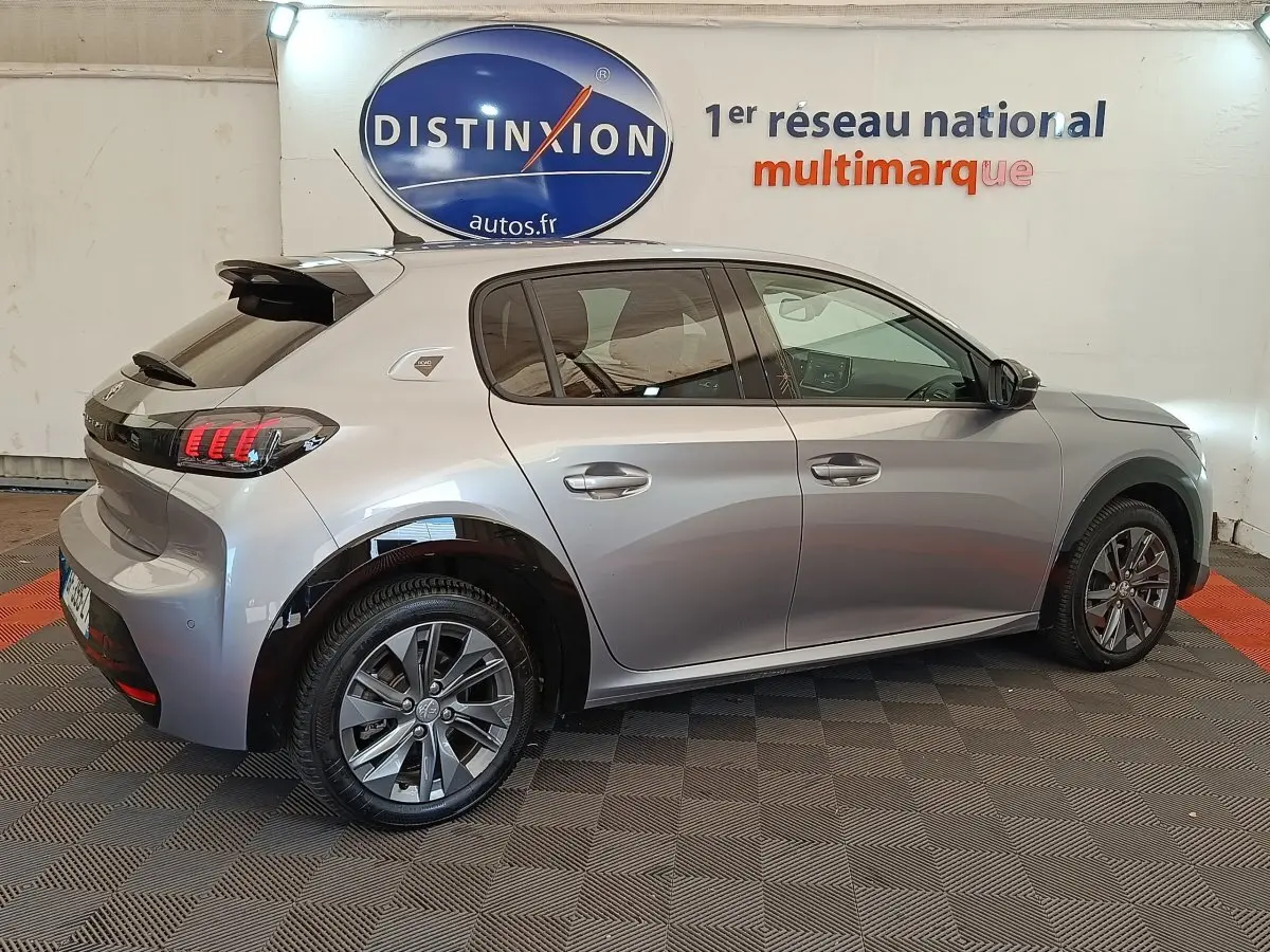 Peugeot 208 électrique gris clair vue de profil côté gauche, avec jantes alliage et feux arrière LED distinctifs.