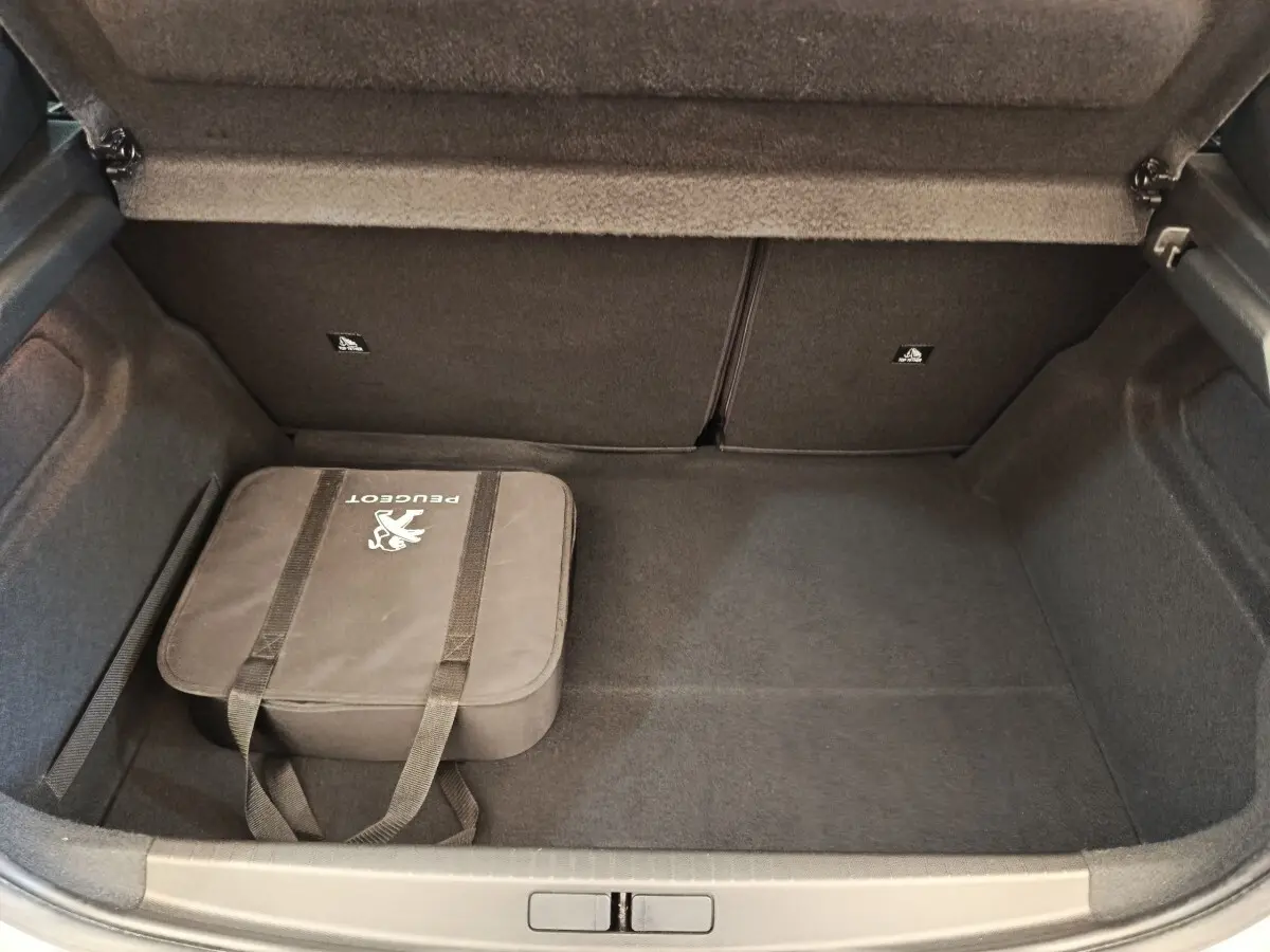 Coffre ouvert de la Peugeot 208 Electrique gris clair, montrant un sac Peugeot noir à l'intérieur.
