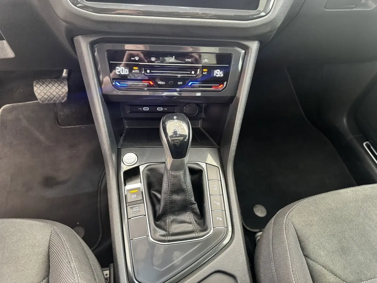 Vue intérieure centrée sur la console centrale du Volkswagen Tiguan gris clair, avec levier de vitesse automatique et commandes climatisation.