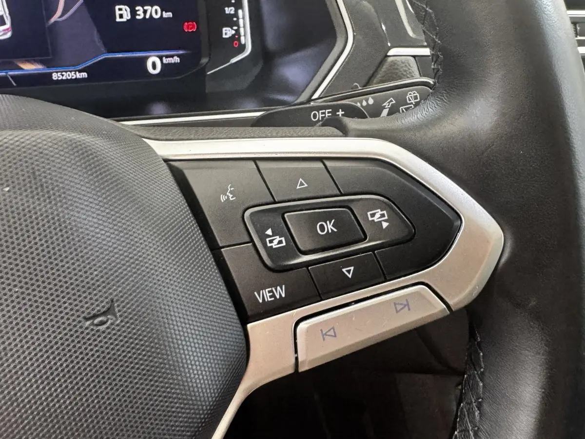 Gros plan sur les commandes multifonctions à droite du volant cuir noir du Volkswagen Tiguan gris clair, tableau de bord digital en arrière-plan.