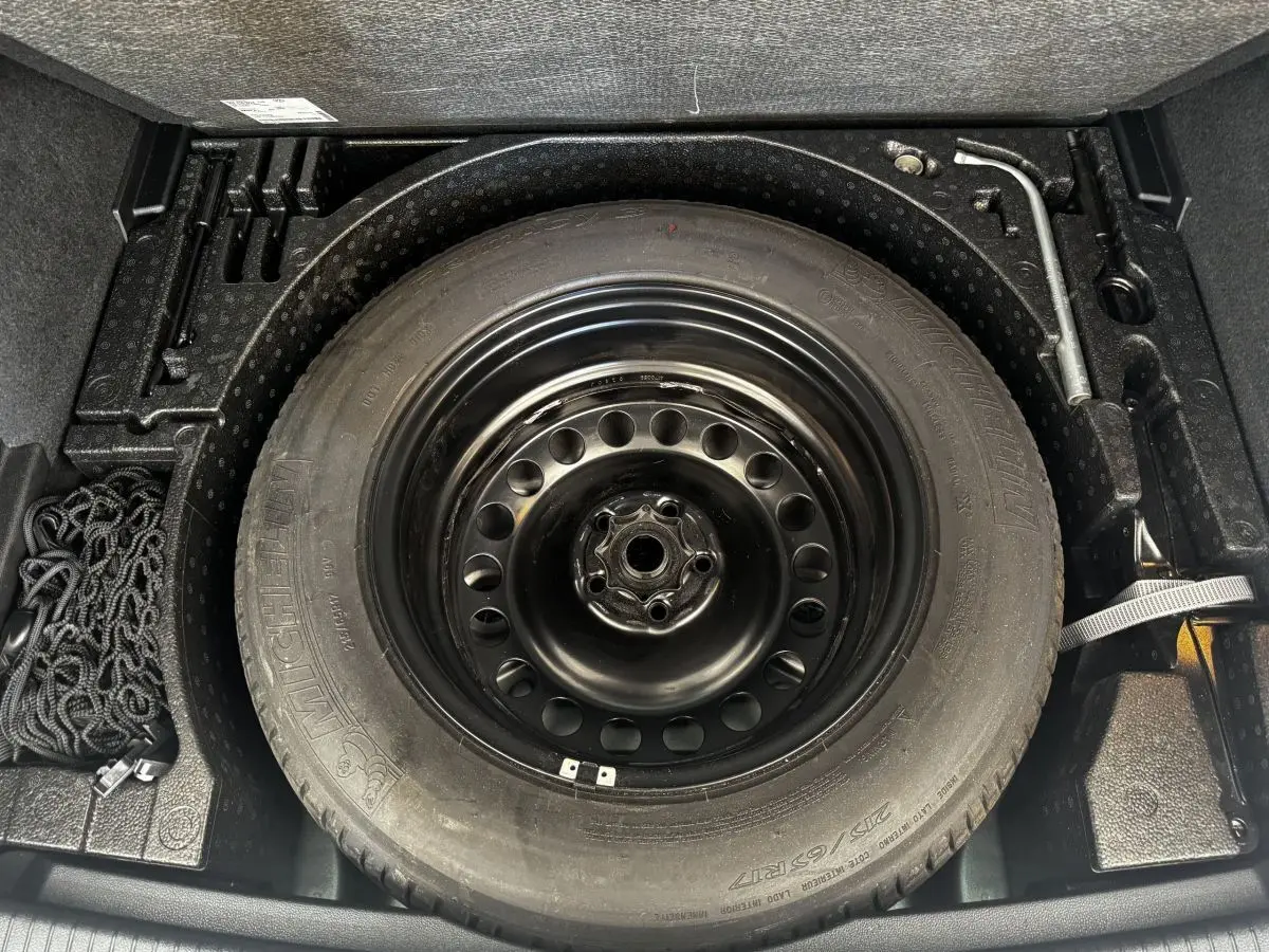 Vue plongeante sur la roue de secours noire et les outils dans le coffre du Volkswagen Tiguan gris clair 2021.