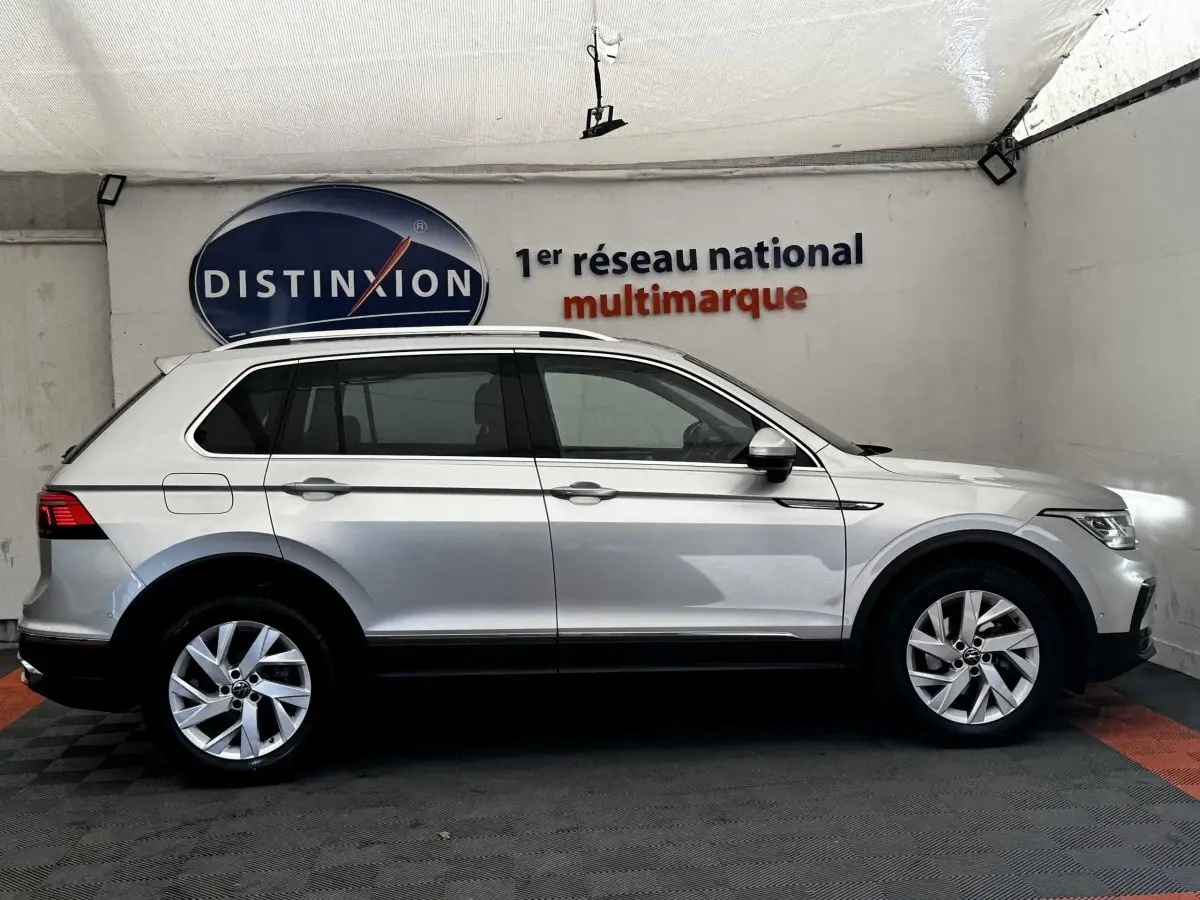 Vue latérale droite d'un Volkswagen Tiguan gris clair 2021 dans un showroom avec logo Distinxion en arrière-plan.