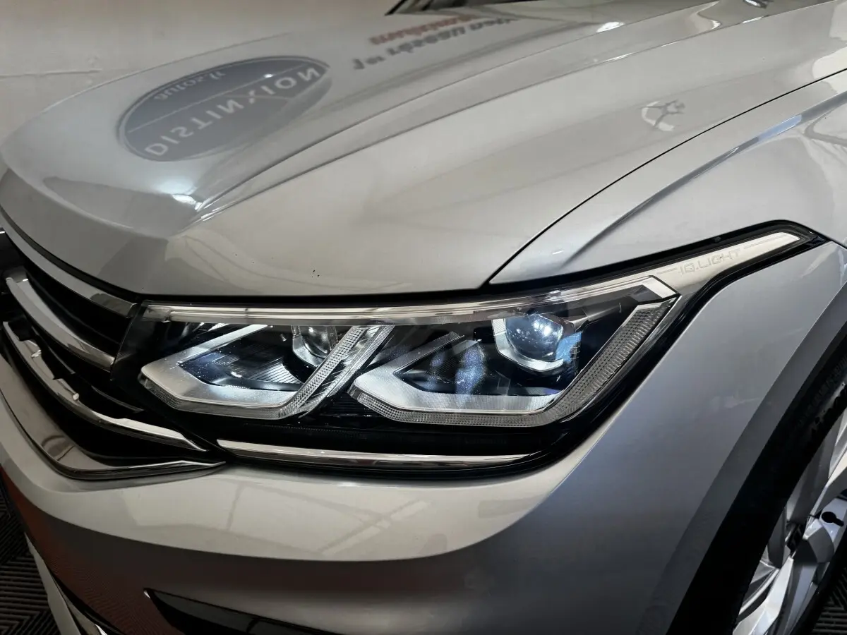 Gros plan sur le phare avant droit allumé du Volkswagen Tiguan gris clair, mettant en valeur la technologie IQ.Light.