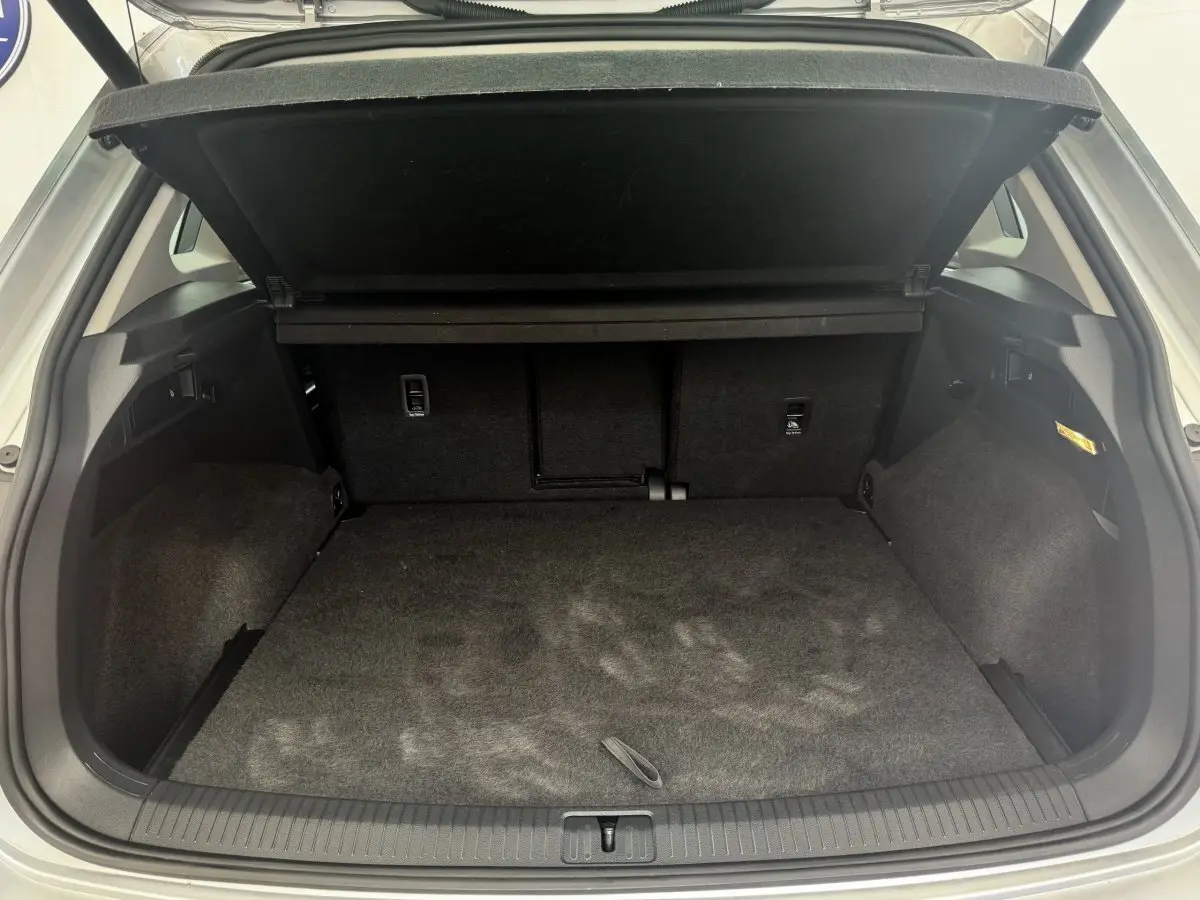 Coffre ouvert vu de l'arrière d'un Volkswagen Tiguan gris clair, espace de chargement propre et tapis noir.