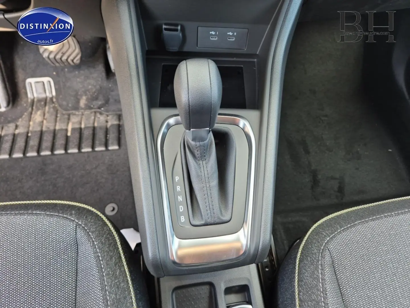 Vue plongeante sur la console centrale avec levier de vitesse automatique noir et sièges tissu gris à surpiqûres vertes.