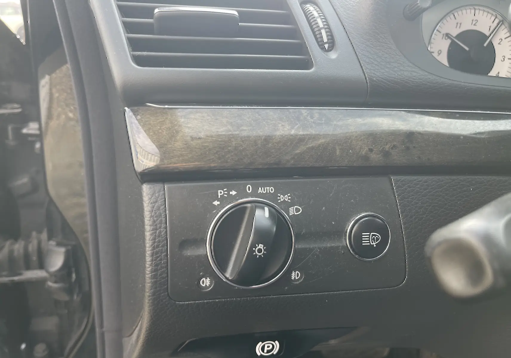 Détail du tableau de bord côté gauche d’une Mercedes Classe E 320 CDI noire de 2003, avec commande des phares et bouton de réglage.