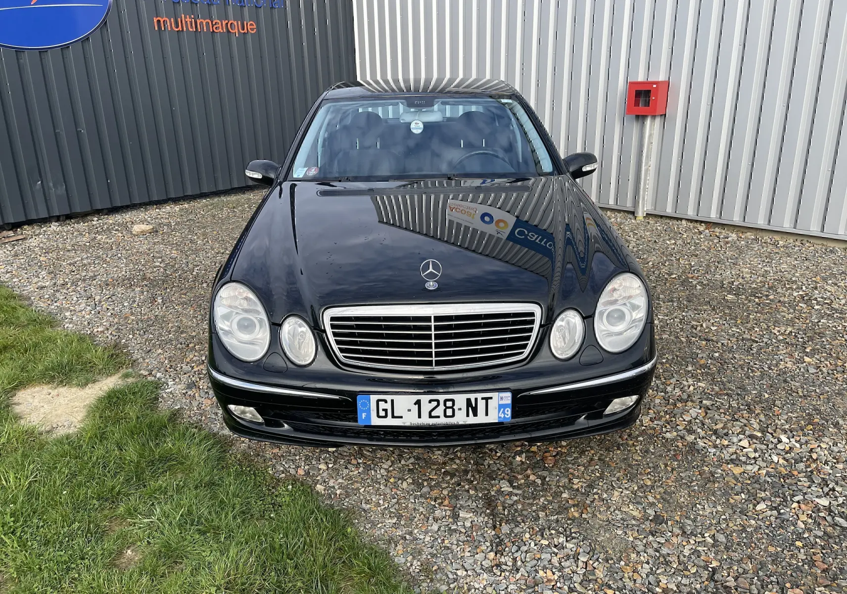 Vue avant d'une Mercedes Classe E noire de 2003, avec calandre chromée et phares ronds caractéristiques.