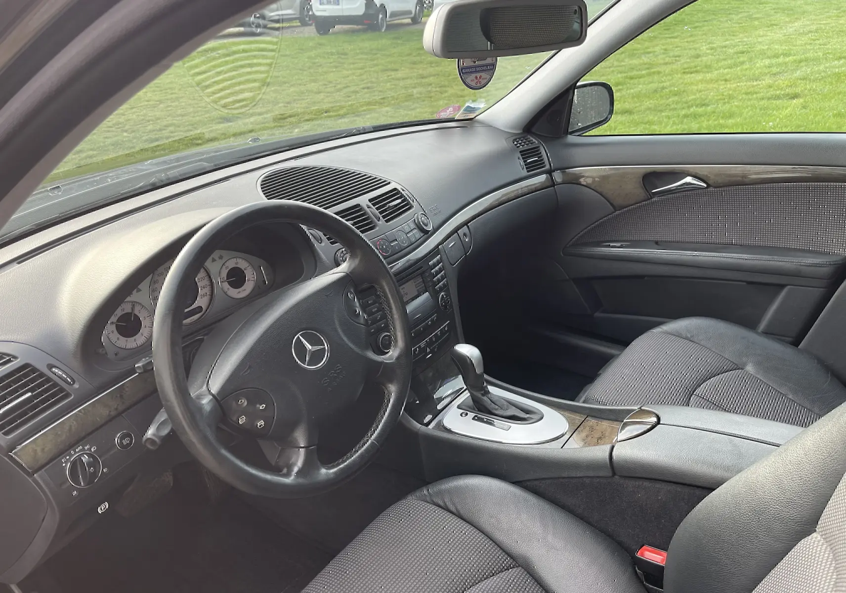 Intérieur de la Mercedes Classe E 320 CDI Elegance 2003, vue côté conducteur, tableau de bord noir avec inserts bois et boîte auto.