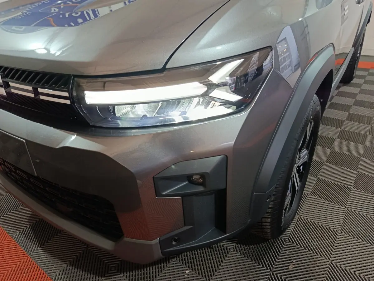 Gros plan sur l'avant droit gris foncé du Dacia Bigster 2025, mettant en valeur le phare LED et la calandre noire.