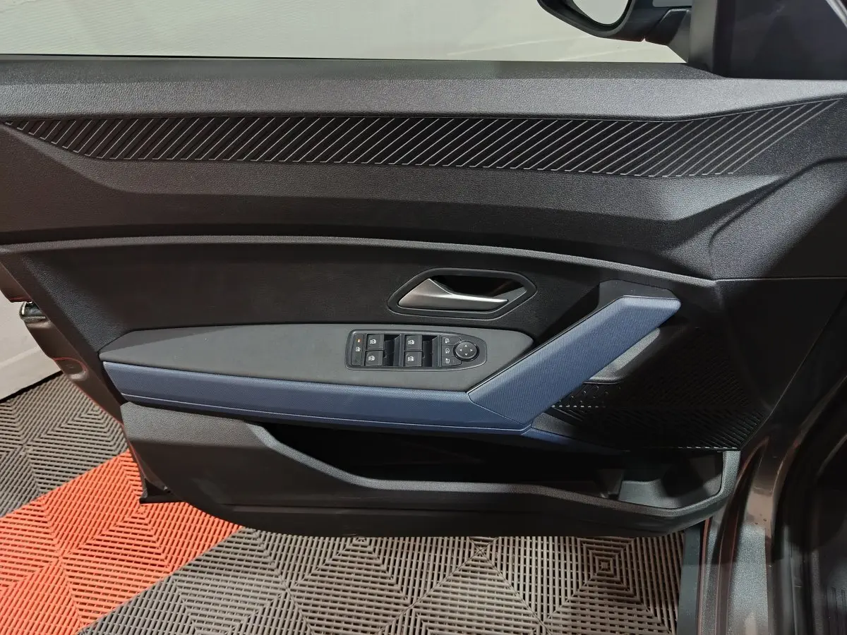 Vue intérieure côté gauche de la porte avant grise foncée du Dacia Bigster avec commandes électriques des vitres et poignée bleue.