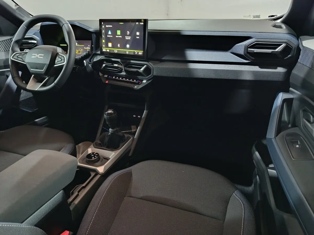 Vue intérieure côté conducteur du tableau de bord et console centrale du Dacia Bigster gris foncé avec écran tactile et boîte manuelle.