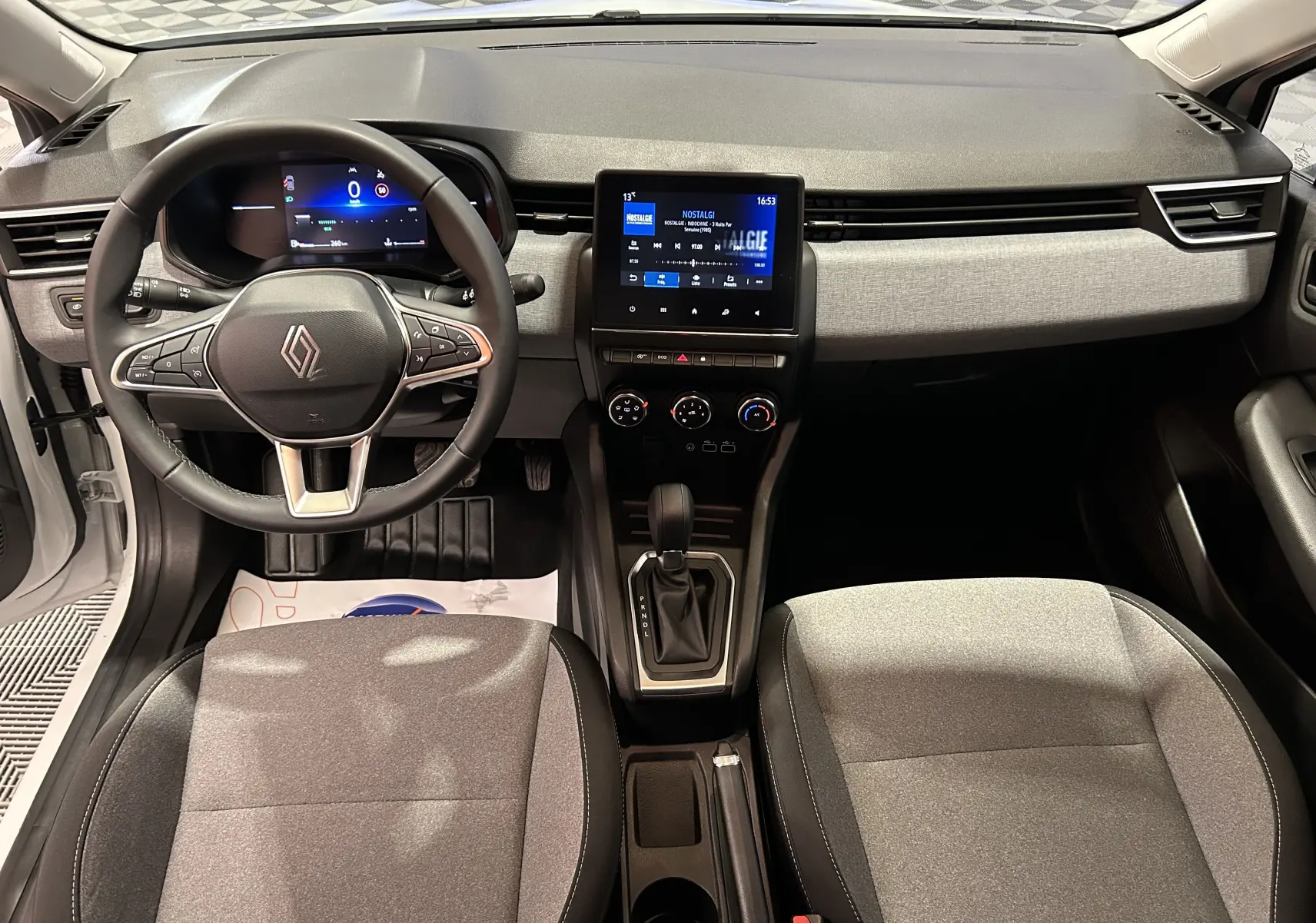 Vue intérieure avant de la Renault Clio V TCE 90ch, tableau de bord noir et gris avec écran tactile central et volant multifonction.