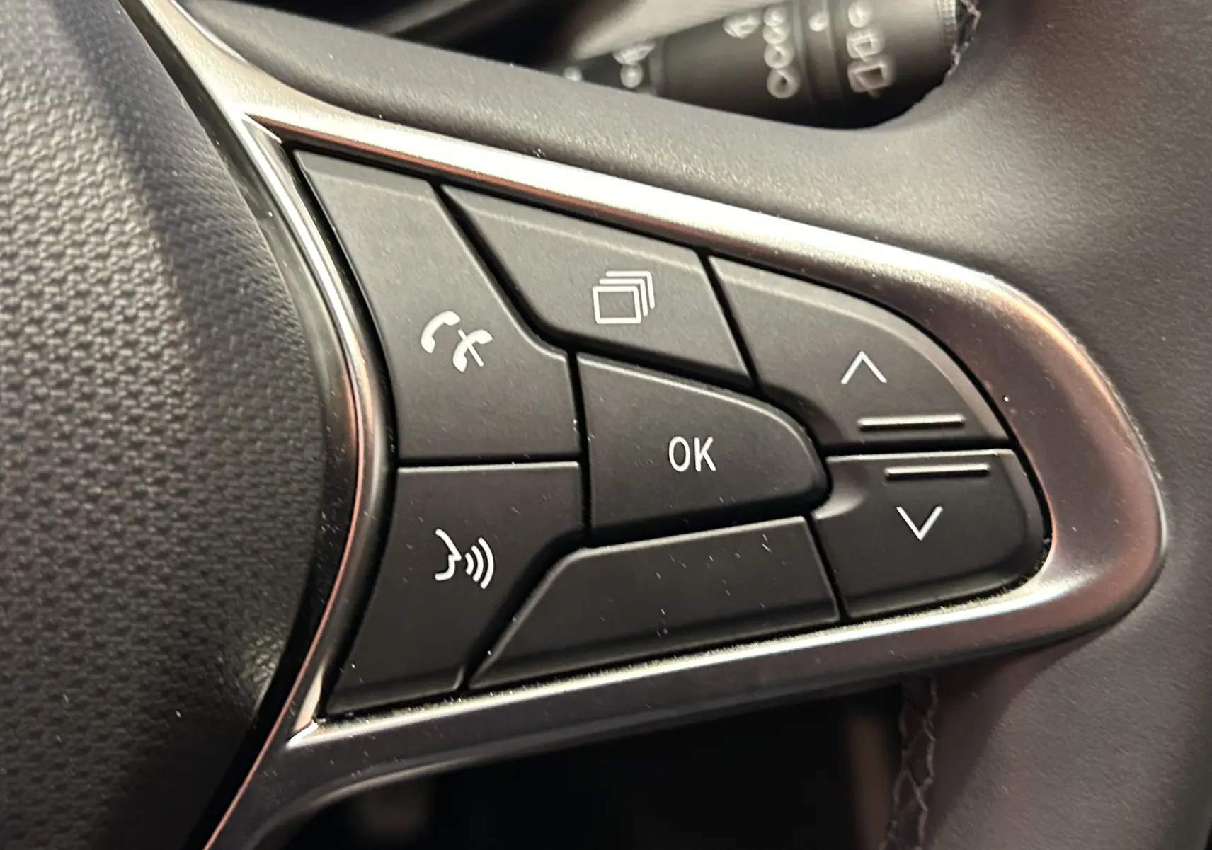 Gros plan sur les commandes multifonctions noires du volant d'une Renault Clio V, finition tissu noir.