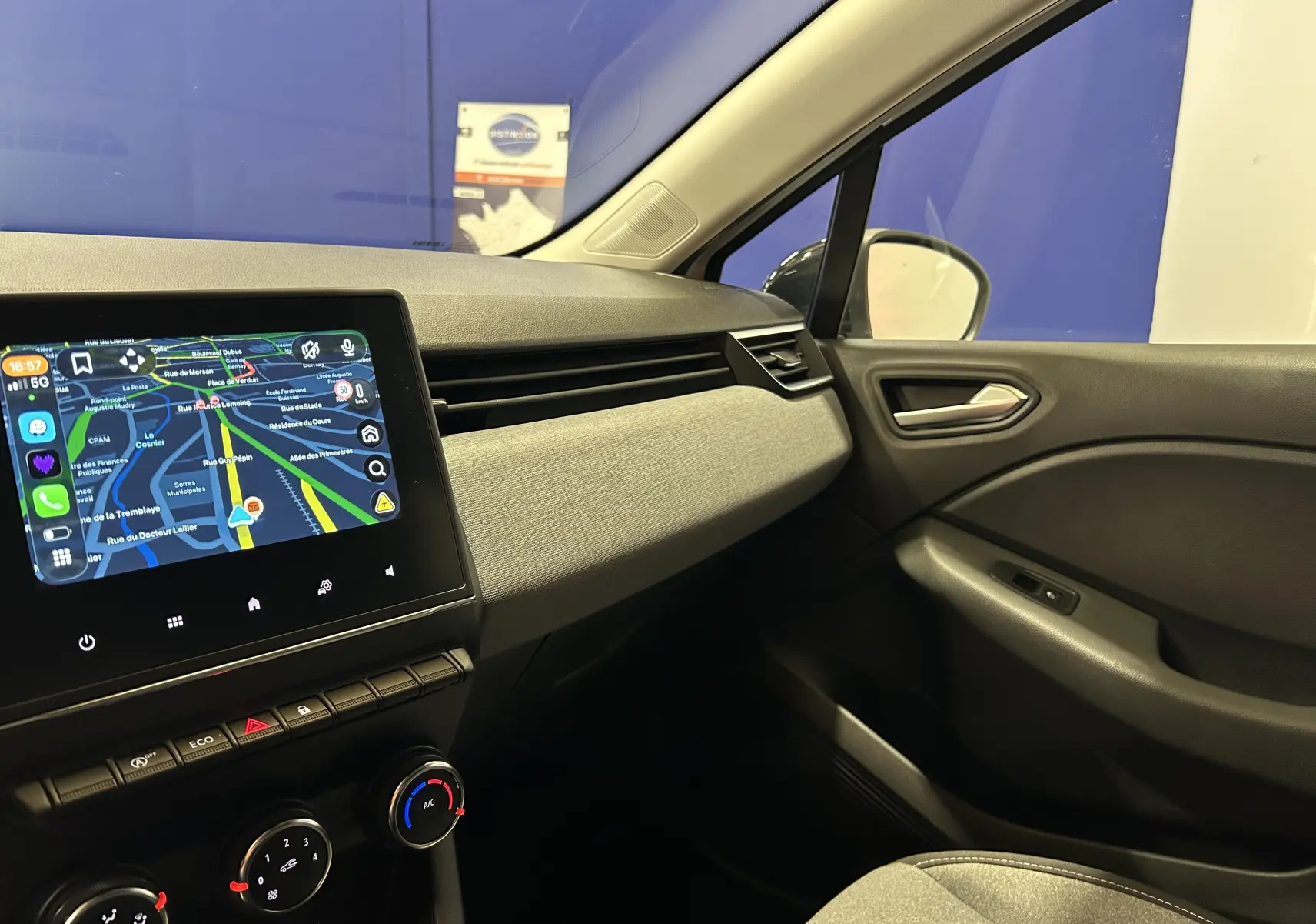 Vue intérieure côté passager de la Renault Clio V blanche, avec tableau de bord moderne et écran tactile affichant la navigation.