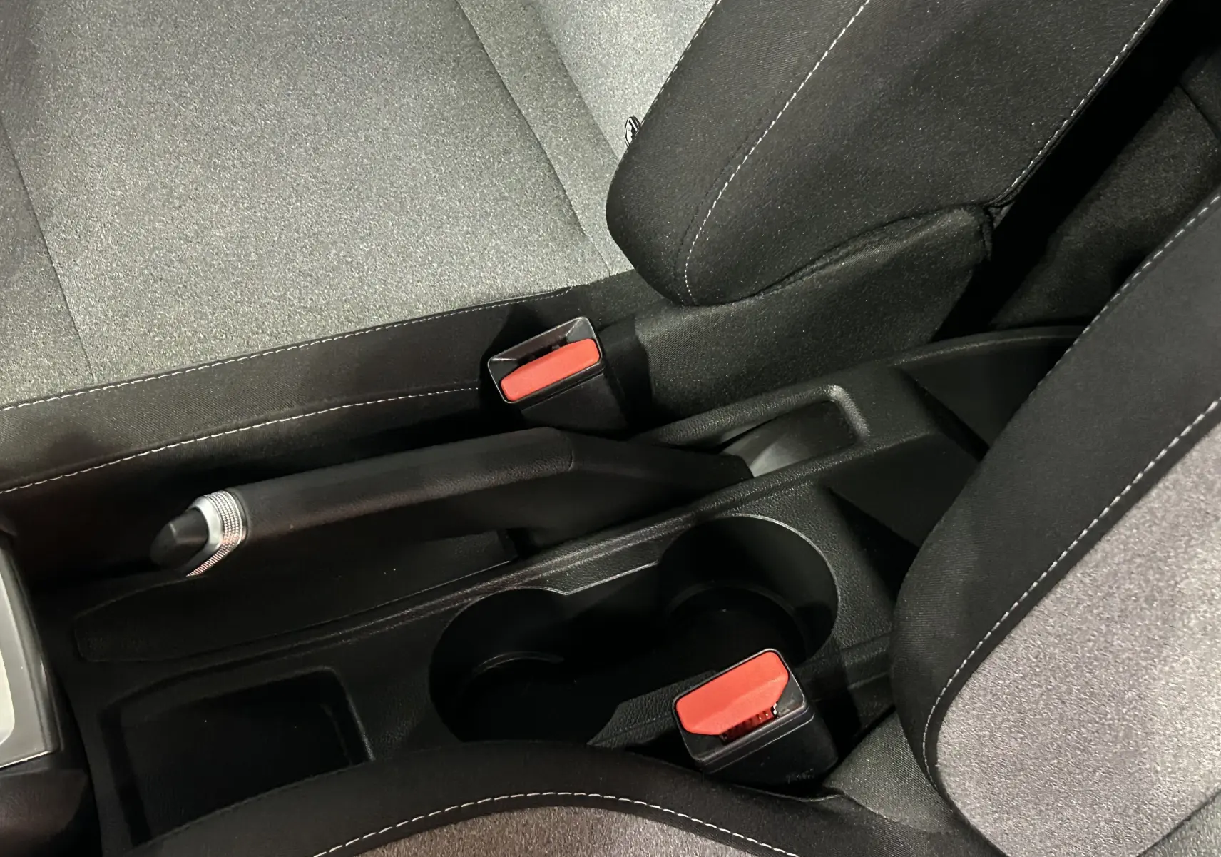 Gros plan intérieur sur la console centrale noire de la Renault Clio V blanche, montrant frein à main et ceintures rouges.