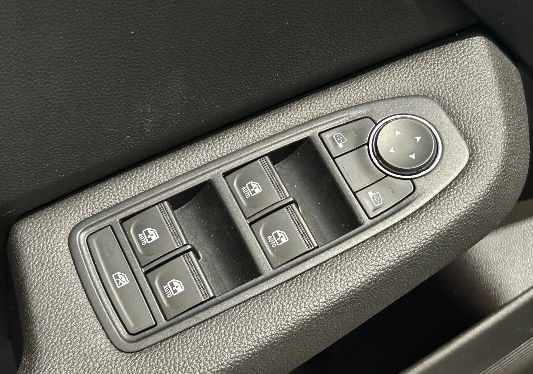 Gros plan sur les commandes de lève-vitres et réglage des rétroviseurs côté conducteur d'une Renault Clio V blanche.