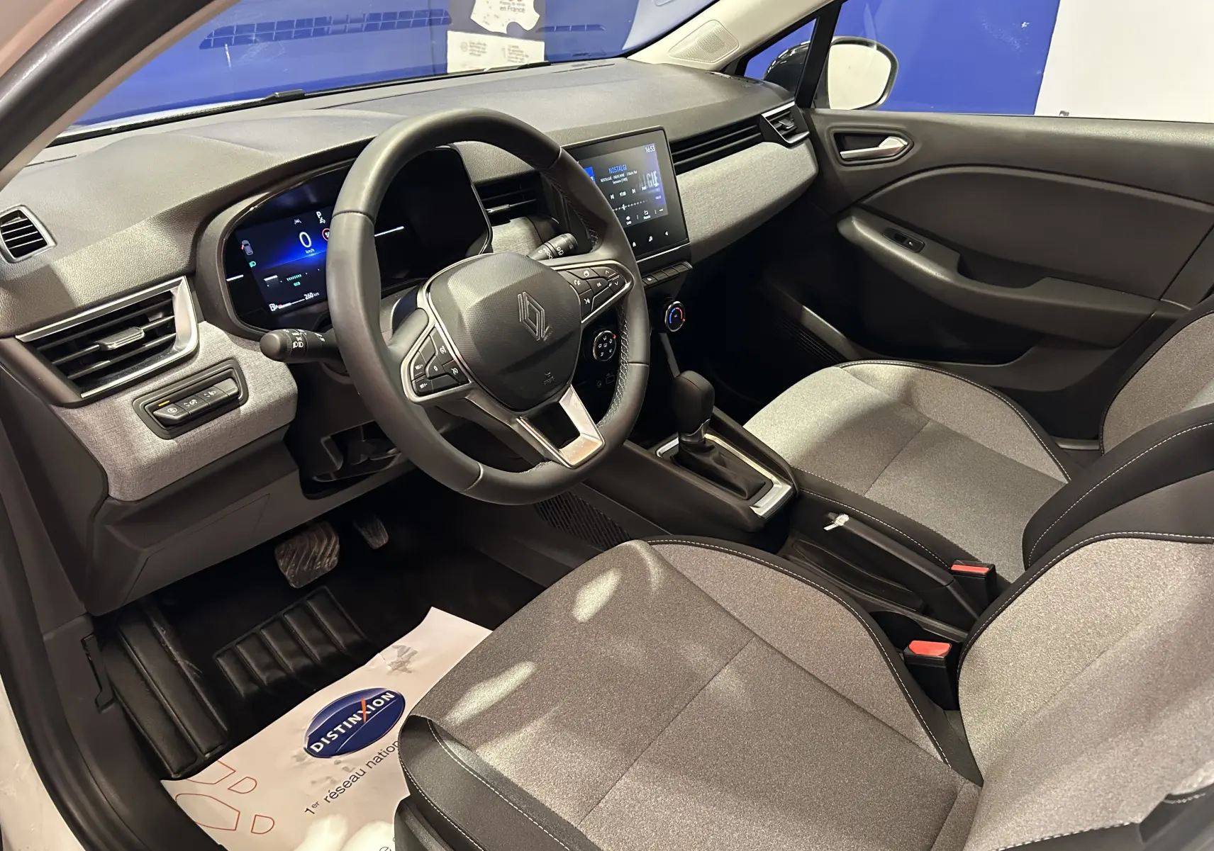 Vue intérieure côté conducteur de la Renault Clio V TCE 90CH avec tableau de bord numérique et sellerie tissu gris.