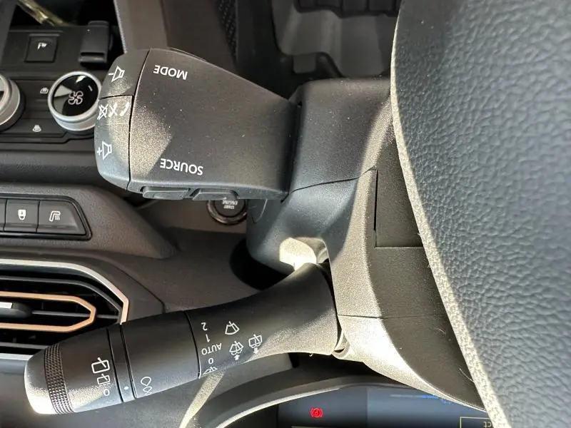 Gros plan sur les commandes au volant du DACIA JOGGER blanc, mettant en valeur les leviers multifonctions et le tableau de bord.