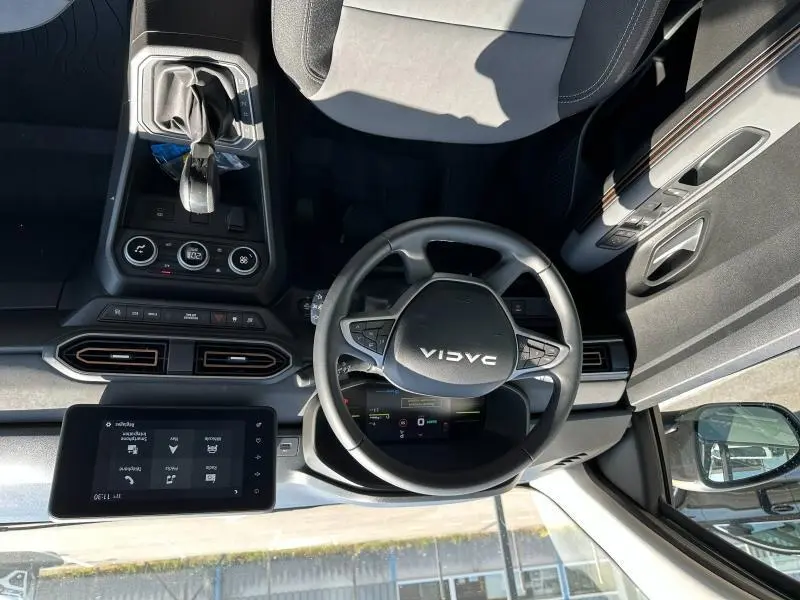 Vue intérieure du poste de conduite du Dacia Jogger blanc, volant multifonctions et écran tactile central visible.
