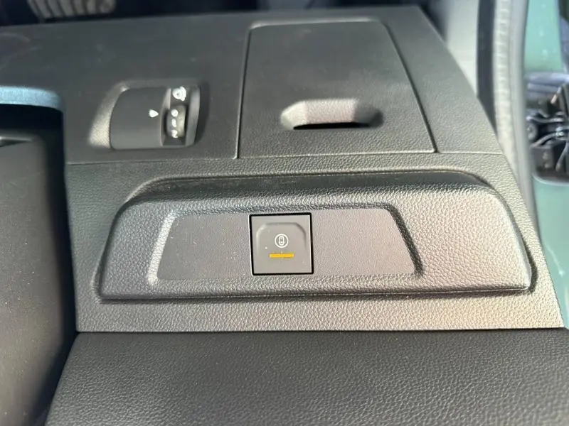 Gros plan sur la commande de frein de stationnement électrique noire dans l'habitacle du Dacia Jogger blanc.