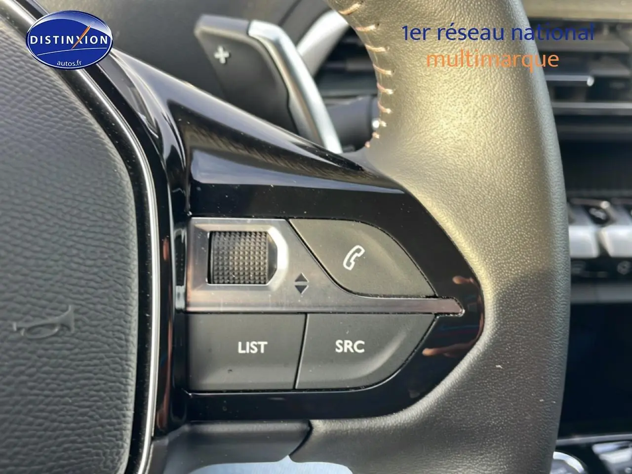 Gros plan sur les commandes audio au volant cuir noir du Peugeot 3008 hybride 2024, côté gauche.