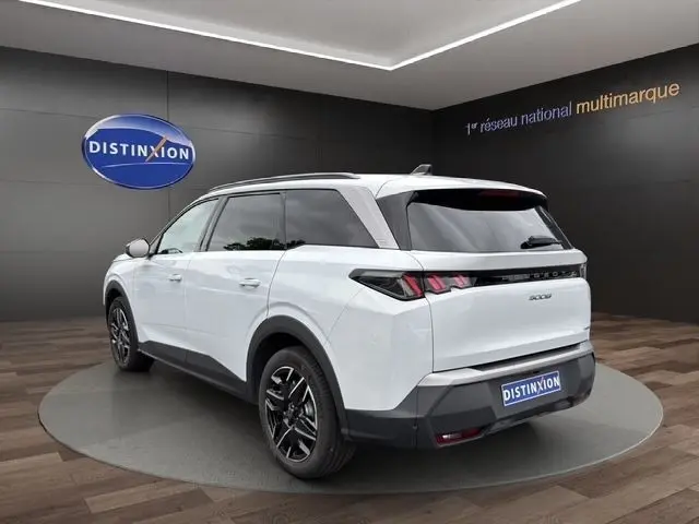 Vue 3/4 arrière droite d'un Peugeot 5008 blanc 2025 avec toit noir et feux arrière LED distinctifs dans un showroom.