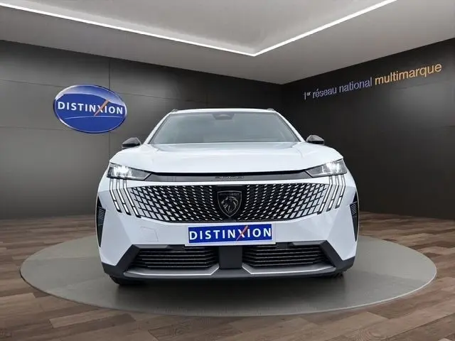 Vue frontale du Peugeot 5008 blanc 2025 avec calandre distinctive et phares LED allumés dans un showroom.