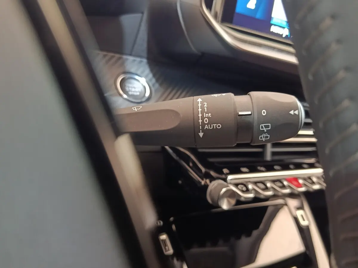 Gros plan sur la commande d’essuie-glace à gauche du volant dans l’habitacle noir d’une Peugeot 208 Electrique gris clair.