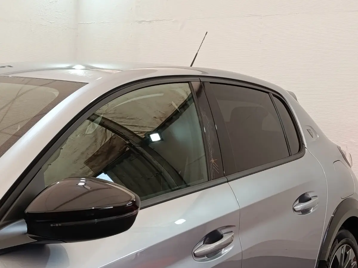 Vue latérale gauche rapprochée d’une Peugeot 208 Electrique Roadtrip gris clair avec rétroviseur noir brillant.