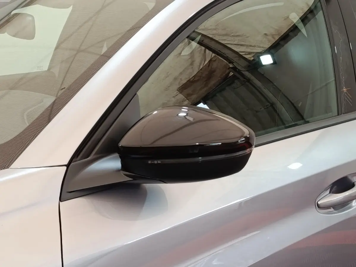 Rétroviseur côté gauche noir brillant sur Peugeot 208 électrique gris clair, vue rapprochée en intérieur.