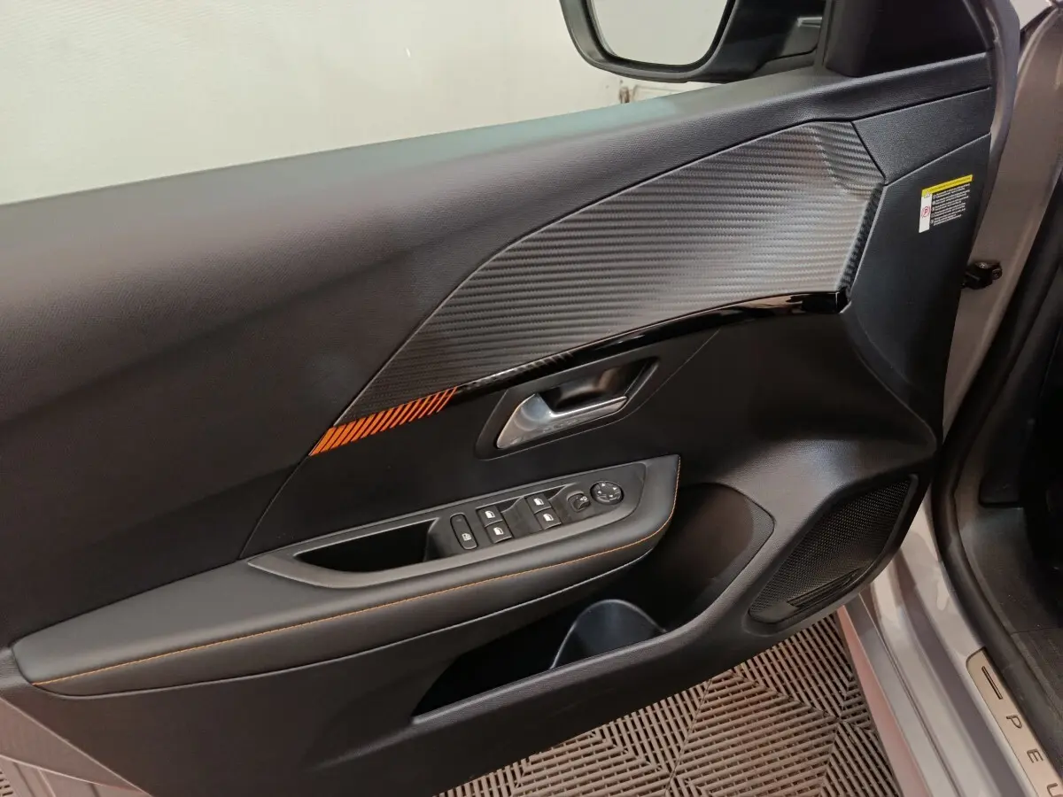 Vue rapprochée de la porte avant gauche gris clair de la Peugeot 208 Electrique ROADTRIP avec insert décoratif noir et orange.