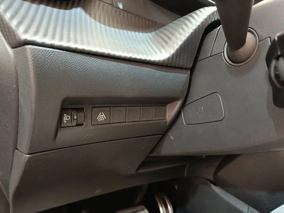 Détail intérieur côté gauche du tableau de bord gris foncé avec commandes d’éclairage et aide à la conduite Peugeot 208 Electrique.