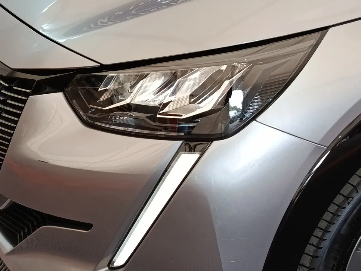 Gros plan sur le phare avant droit LED et la carrosserie gris clair d'une Peugeot 208 Electrique ROADTRIP 2022.