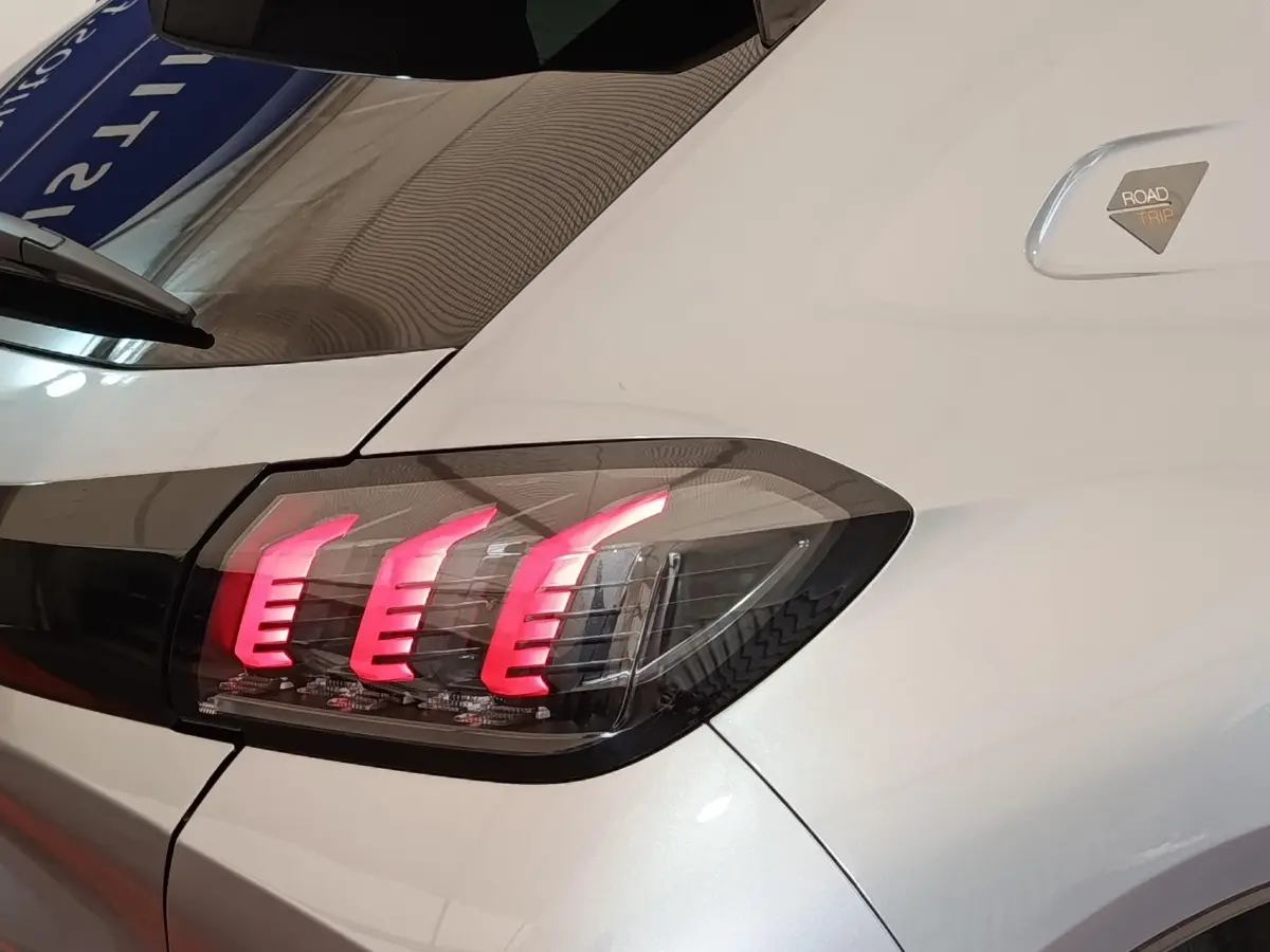 Gros plan sur le feu arrière droit allumé d’une Peugeot 208 Electrique ROADTRIP gris clair, avec badge spécifique visible.