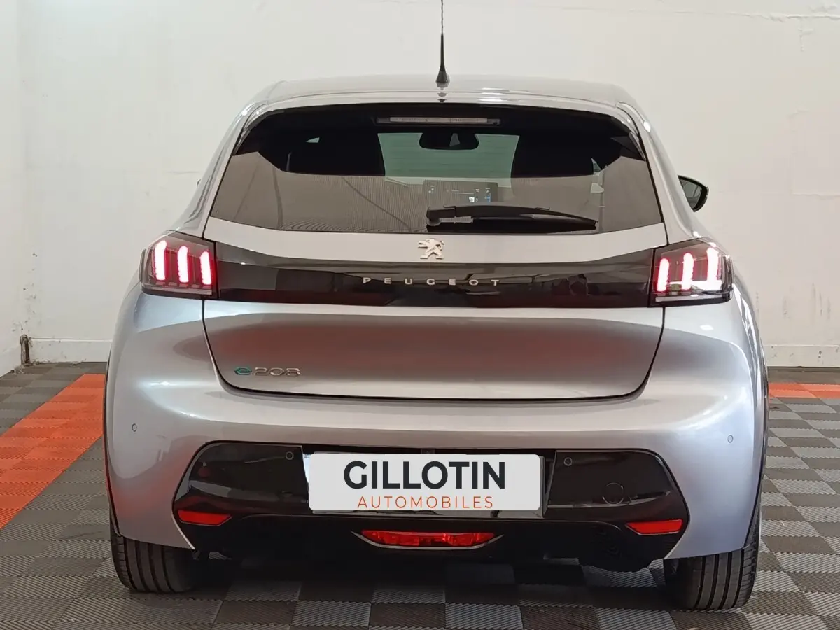 Vue arrière de la Peugeot 208 électrique gris clair avec feux LED distinctifs et logo Peugeot lumineux.